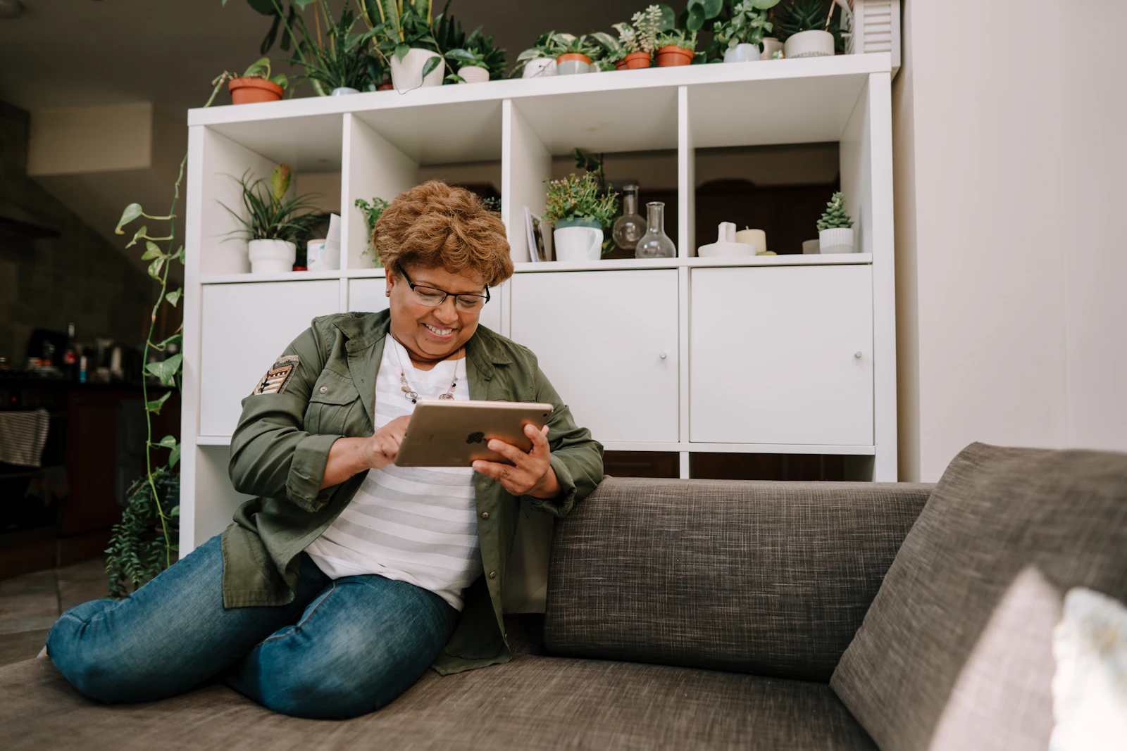 Lächelnde Frau sitzt auf dem Sofa und surft auf einem Tablet