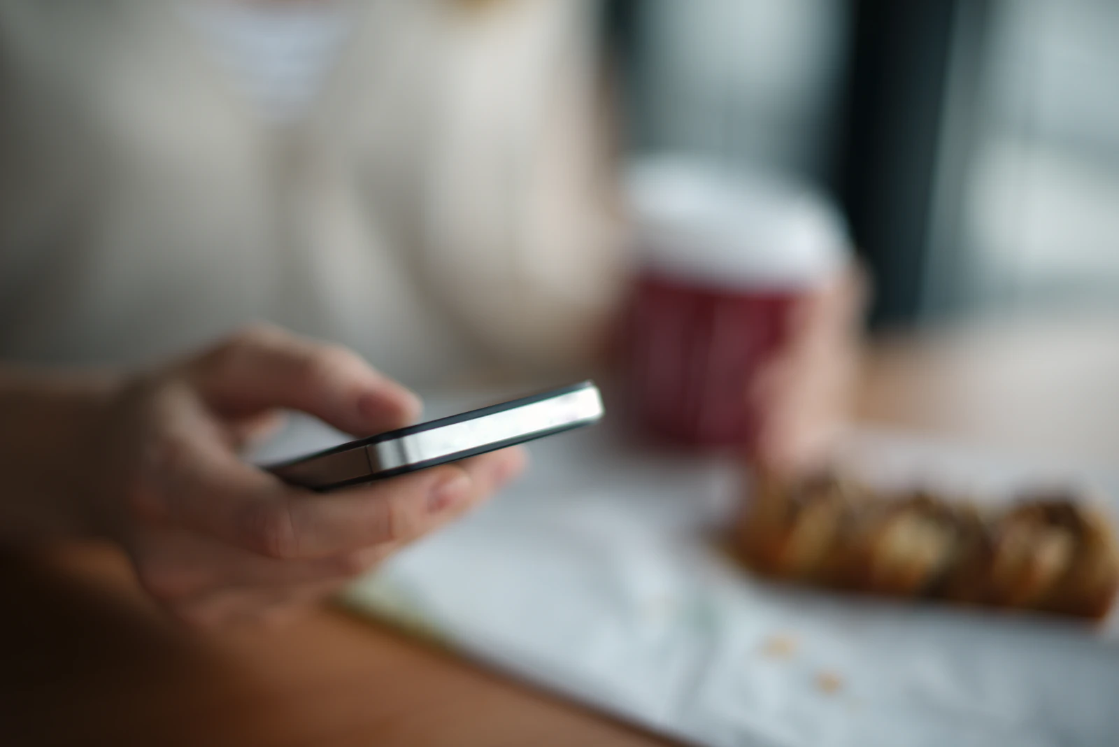 Hand hält ein Smartphone am Frühstückstisch